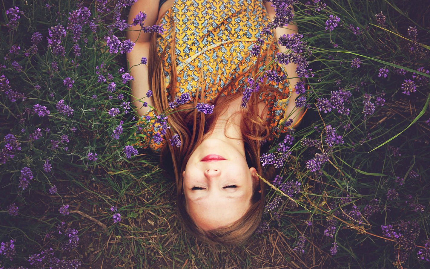 Woman with closed eyes lying in a field of purple lavender flowers