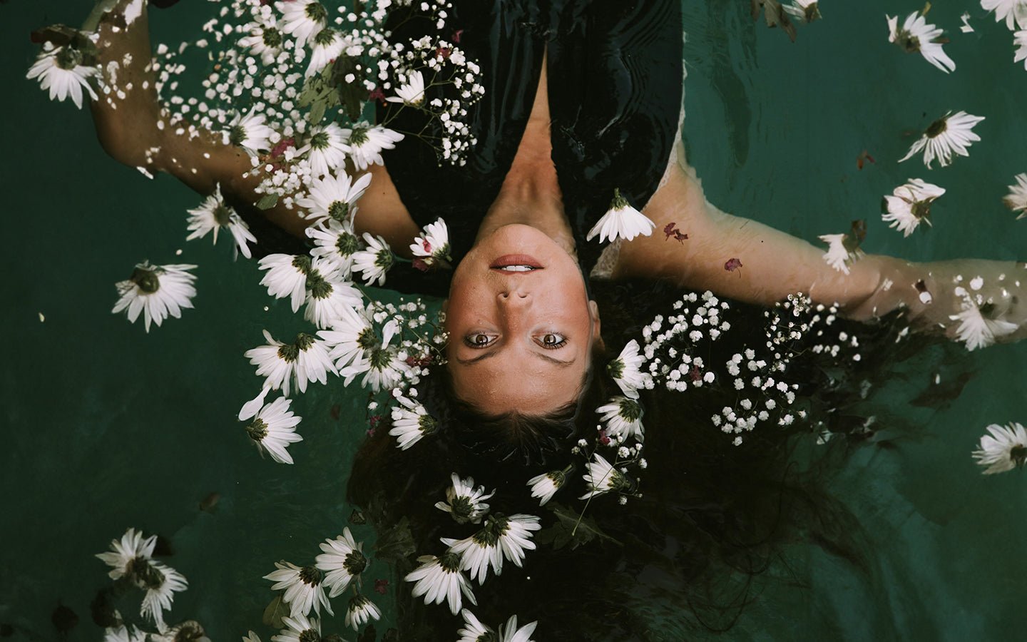 Woman in dark water with white flowers, looking up