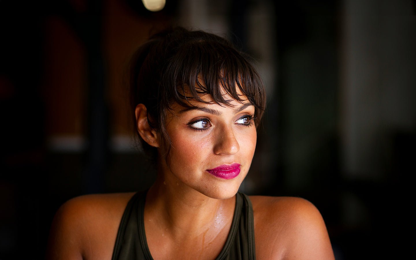 Woman with dark hair and pink lipstick, wearing a green tank top, looking right