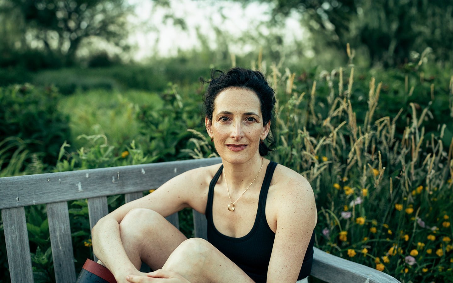 Woman in black tank top on wooden bench in a garden