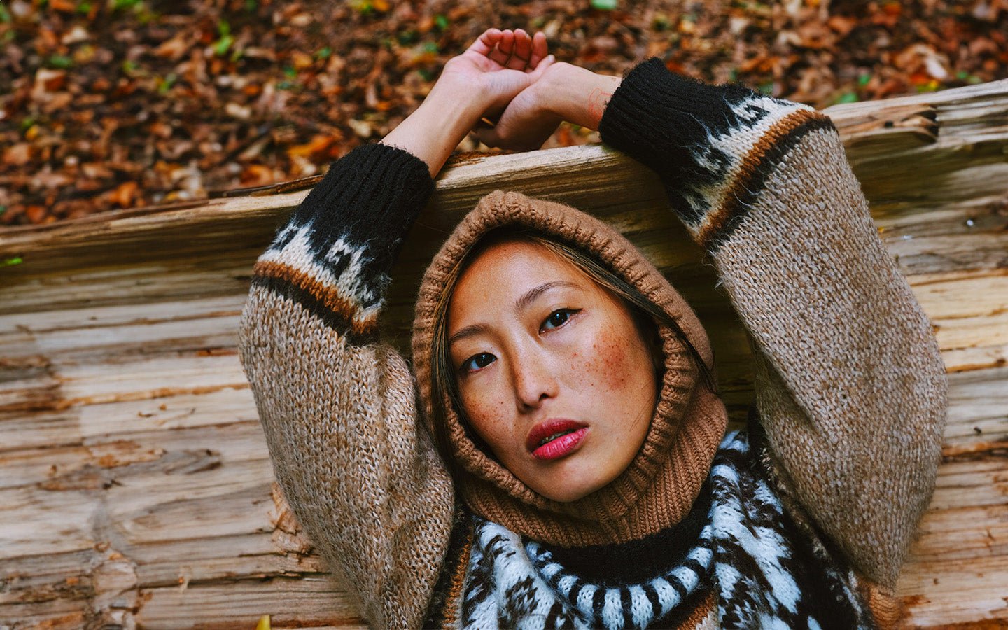 Woman with freckles in a brown hooded sweater lying on a log