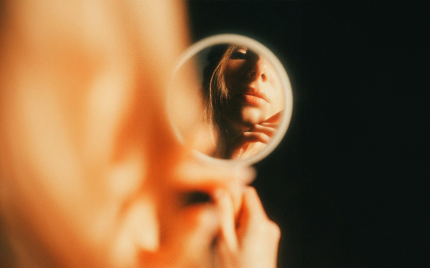 Woman's face reflected in a small mirror, holding it with hands