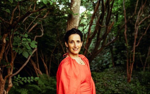 Woman in coral dress smiling in a lush green garden