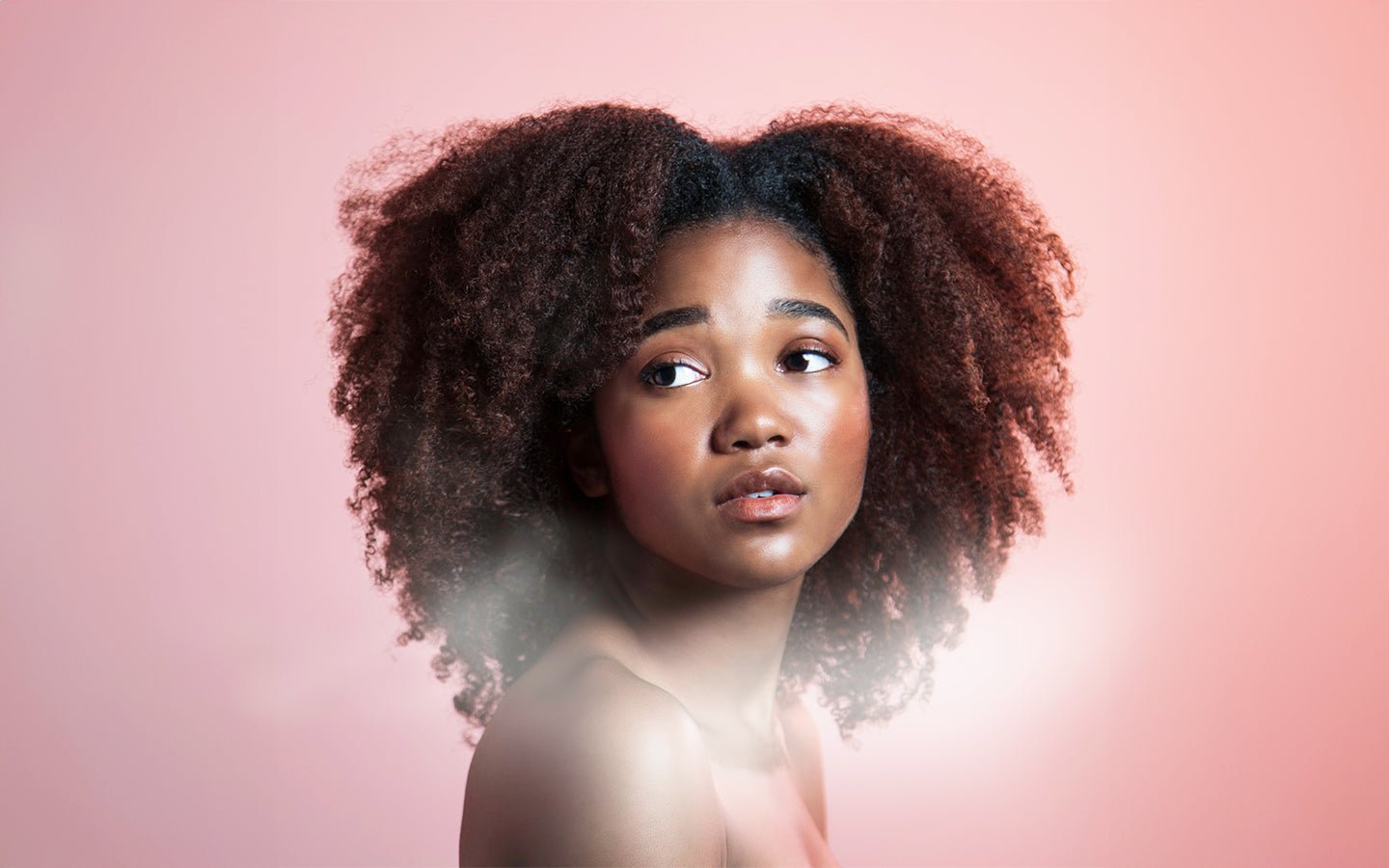 Young Black woman with natural hair looking left on a pink background