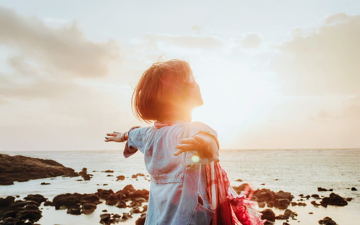 Woman with outstretched arms on a rocky beach at sunset