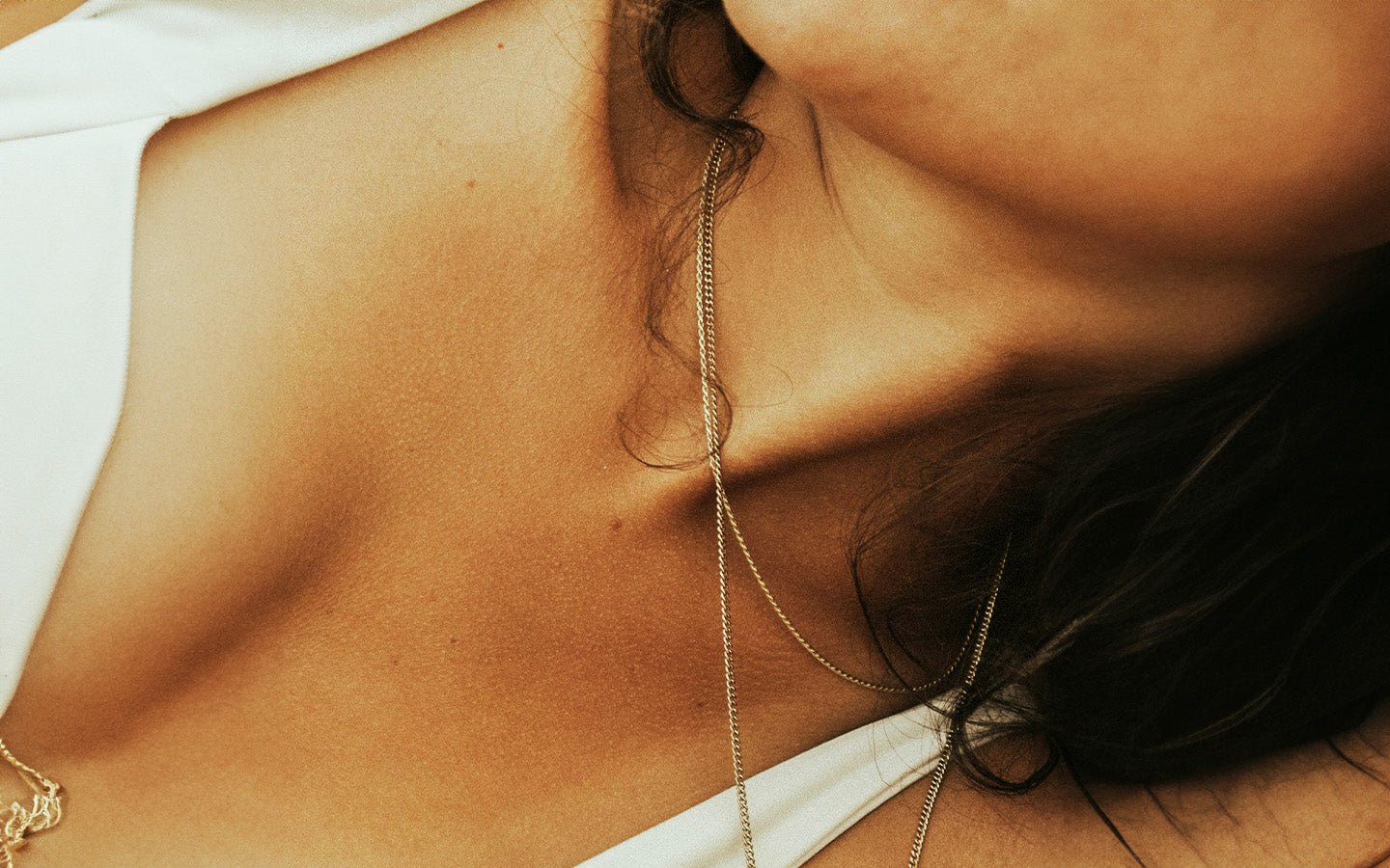 Close-up of a woman's chest and neck with a gold chain and dark hair