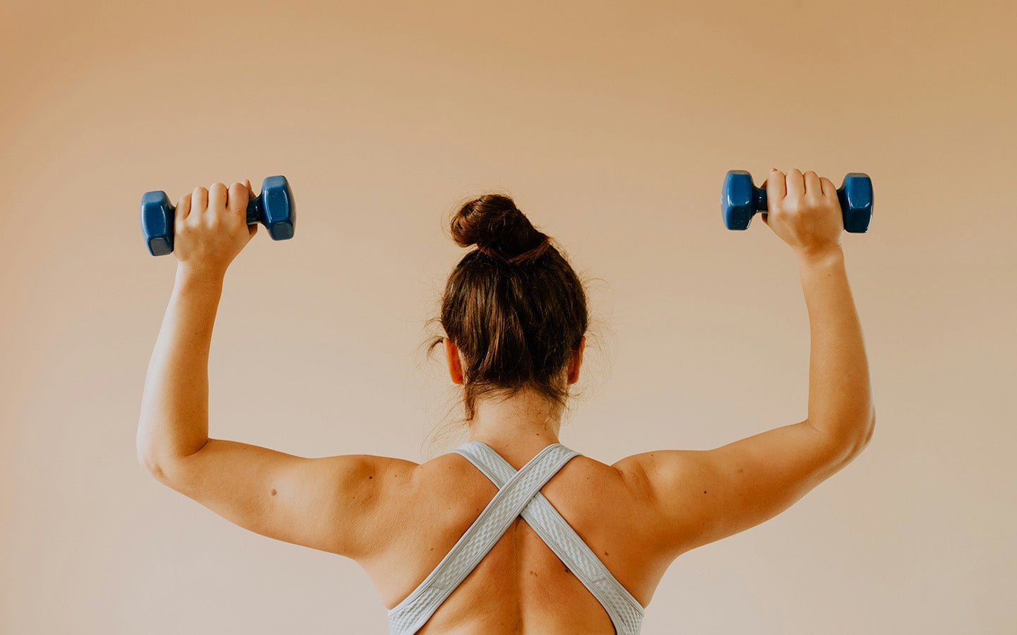 Woman from behind holding blue dumbbells, wearing a light blue sports bra
