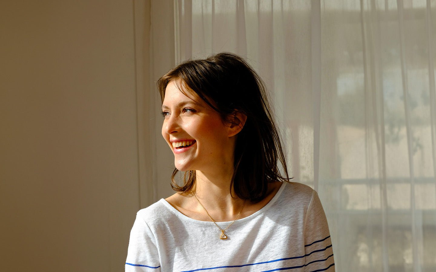 Smiling woman in white and blue striped shirt with gold triangle necklace