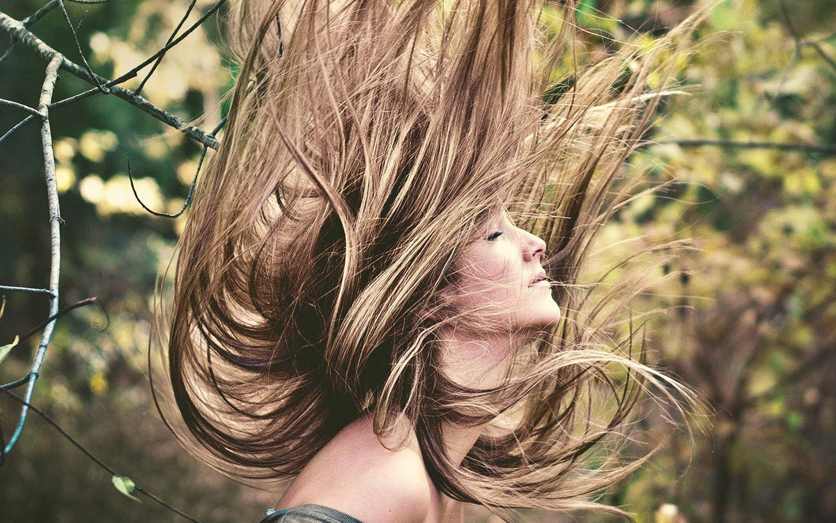 Woman with long brown hair flying up, eyes closed, in a forest