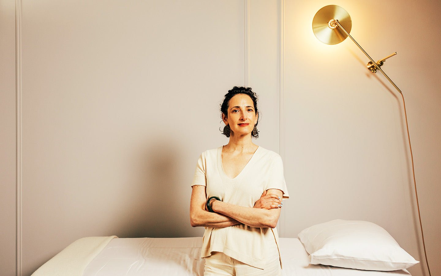 Woman in cream top standing in front of a treatment bed with a gold lamp