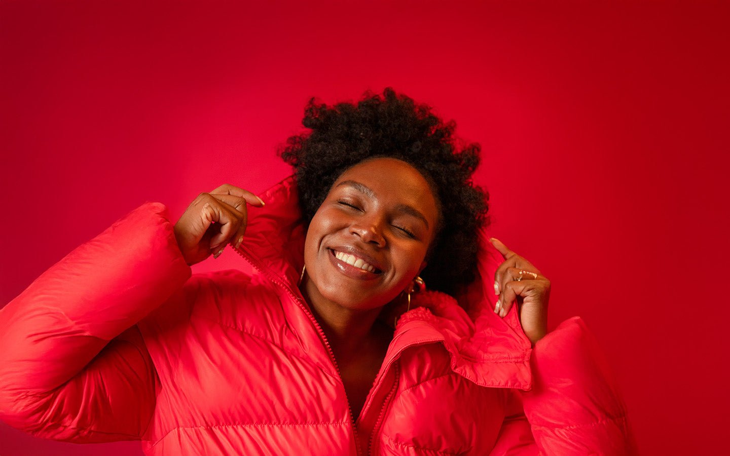 Smiling woman in red puffer jacket against a red background