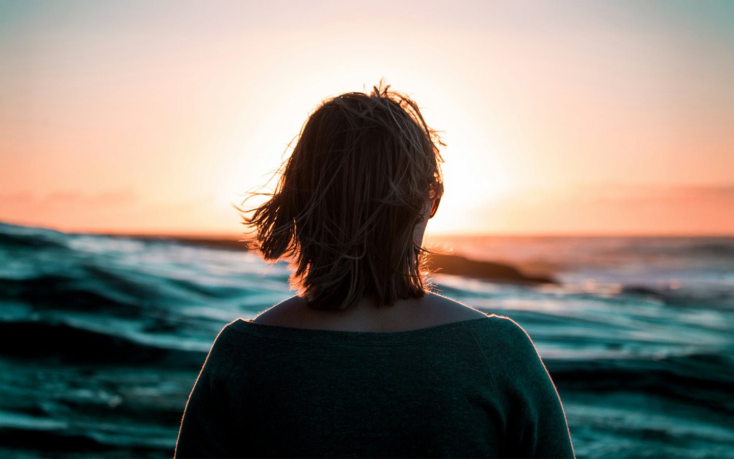 Woman with short hair watching sunset over ocean waves