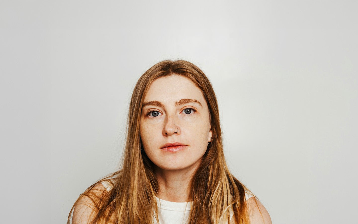 Woman with long brown hair, blue eyes, and a nose ring looking forward