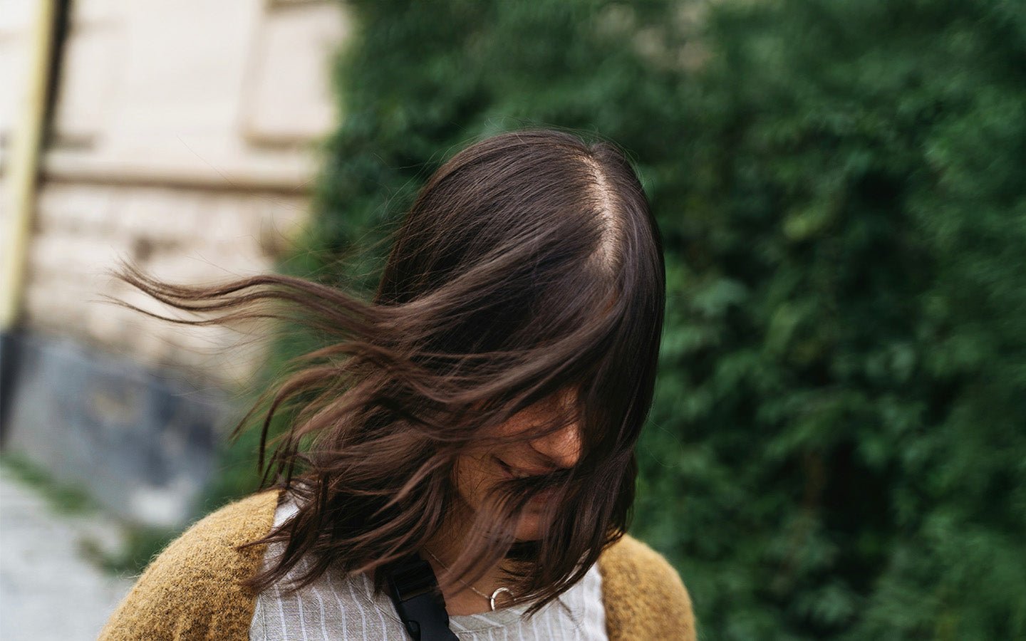 Woman with dark hair blowing in wind, wearing a brown sweater