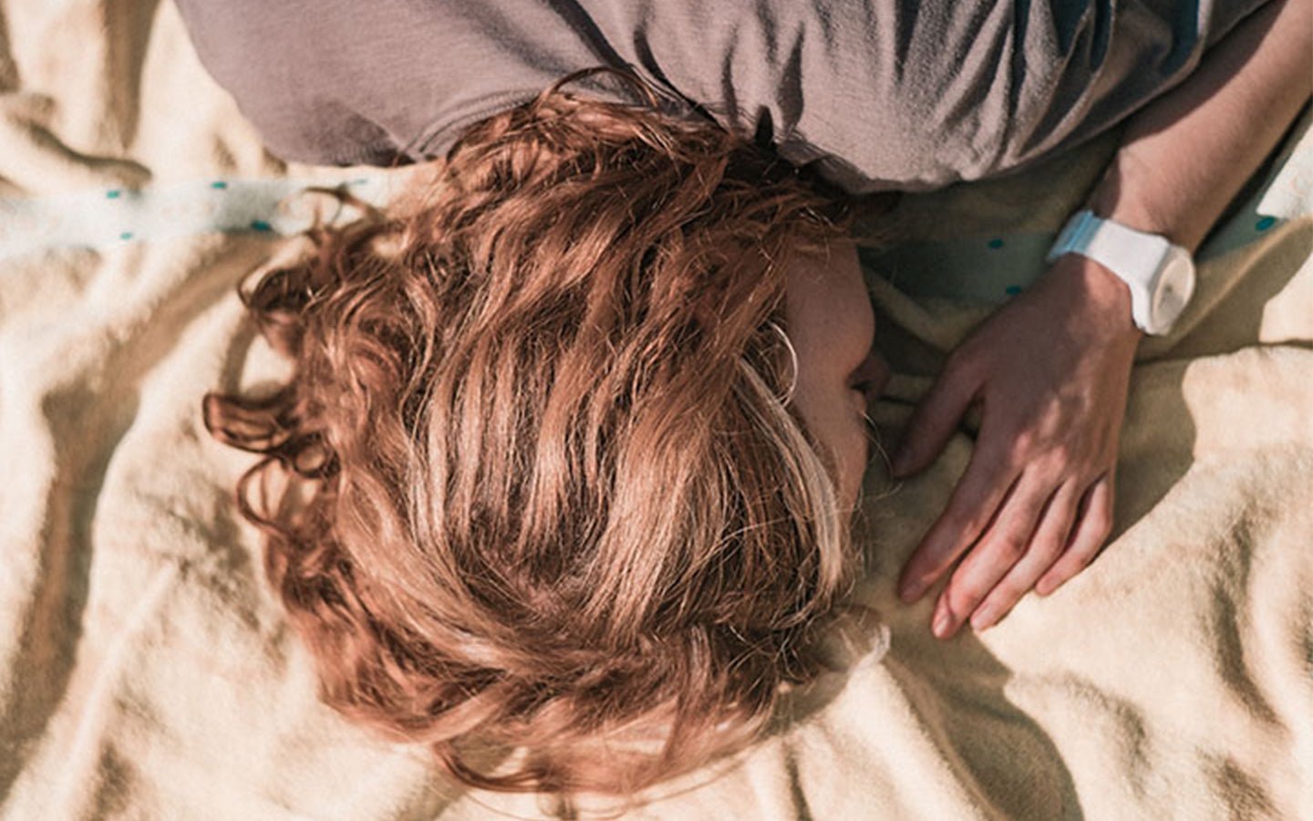 Woman with auburn hair and white watch sleeping on a yellow blanket