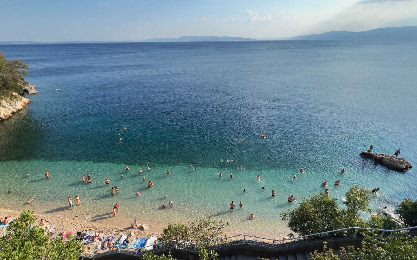 Beach with many people swimming and sunbathing in clear blue water