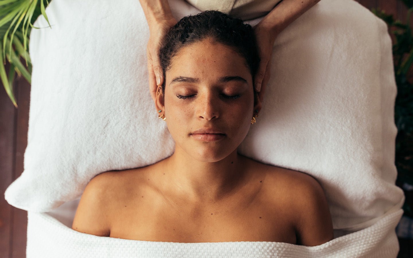 Woman relaxing with eyes closed during a facial spa treatment, hands cradling her head