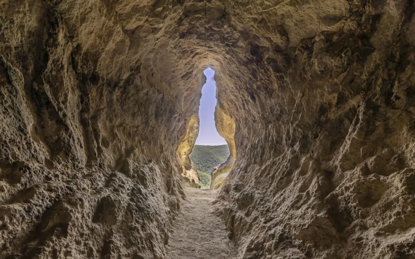 The vulva-shaped opening of Utroba Cave in Bulgaria, seen from inside the passage looking out onto sunlit green hills