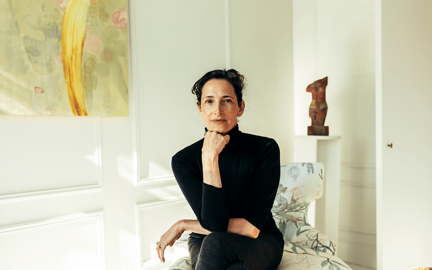 Dr. Catherine in a black turtleneck seated with her hand on her chin in a bright room