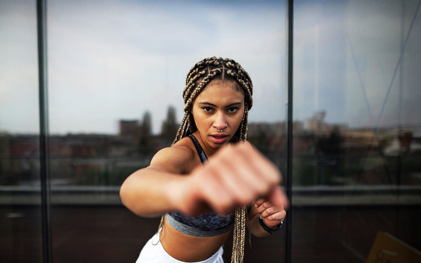 Woman with braided hair in a sports bra, punching towards the camera