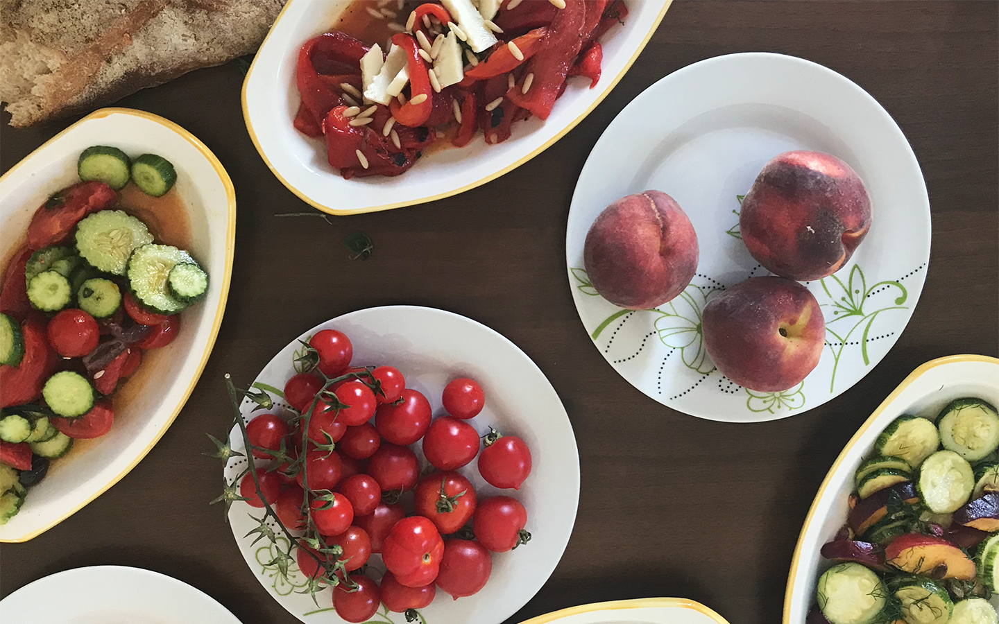 Overhead summer spread of cucumber-tomato salad, roasted peppers, cherry tomatoes, and fresh peaches served at room temperature