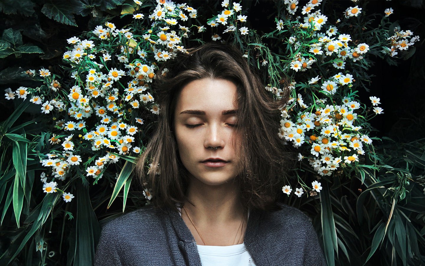 Woman with closed eyes, surrounded by white and yellow daisies and green leaves