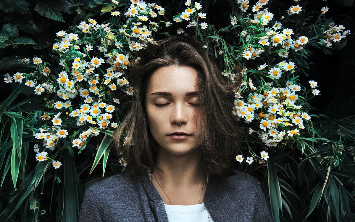 Woman with closed eyes, surrounded by white and yellow daisies and green leaves