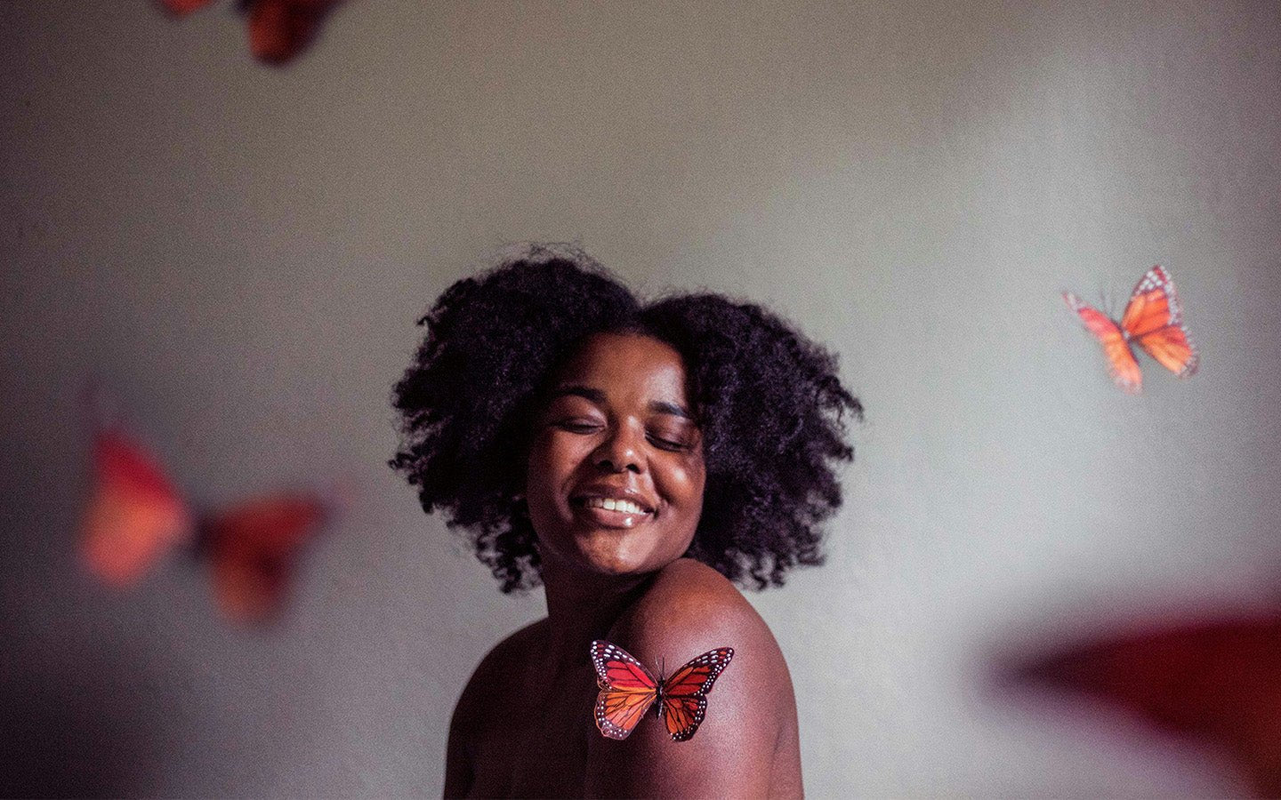 Smiling woman with dark curly hair and a monarch butterfly on her shoulder