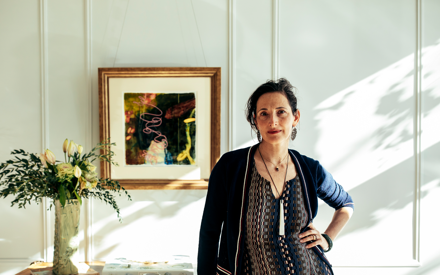 Dr. Catherine in a sunlit white-panelled room, a long pale pendant resting over her heart