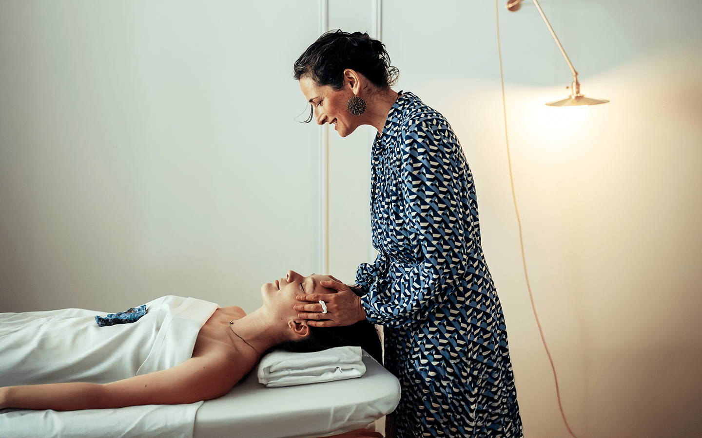 Woman in blue dress performing head massage on client in white