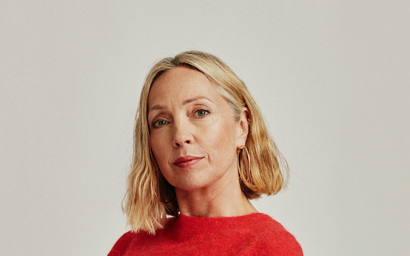Blonde woman in red sweater with gold hoop earrings looking forward
