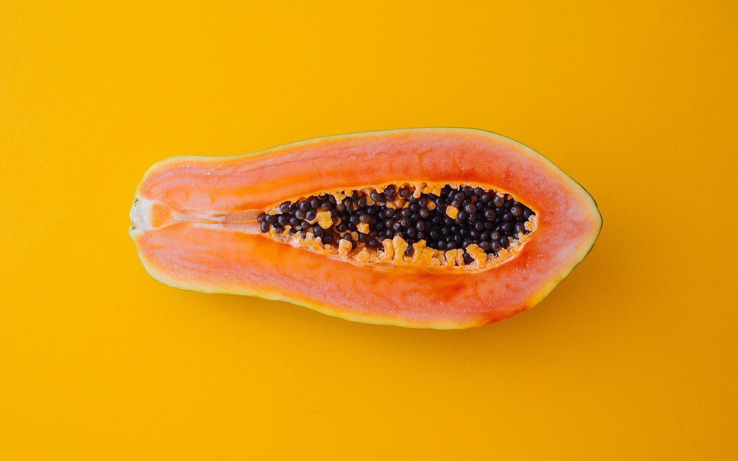 Half a ripe papaya with black seeds on a bright yellow background