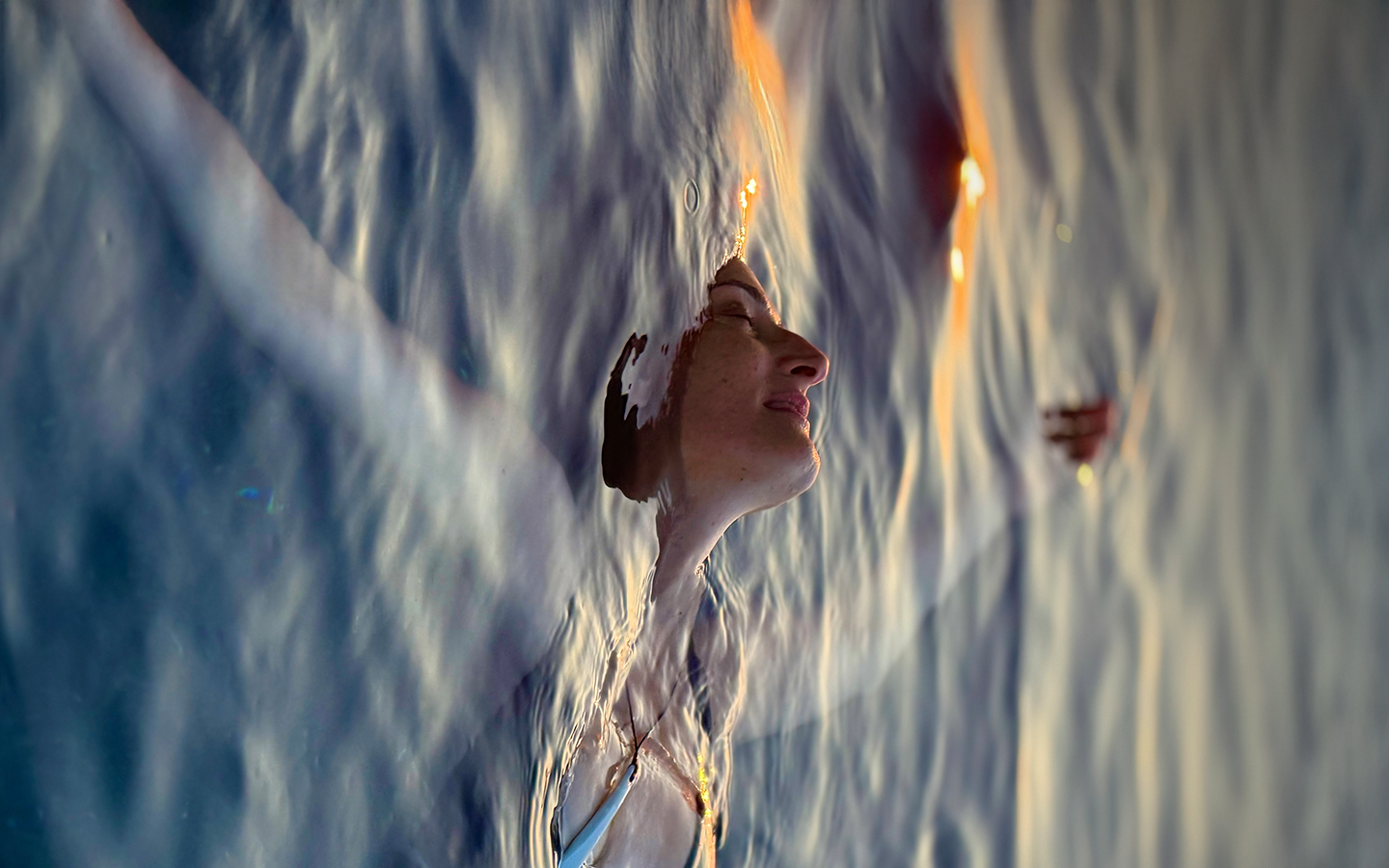 Dr. Catherine floating at sunset, eyes closed and face tilted back, her profile cresting the water