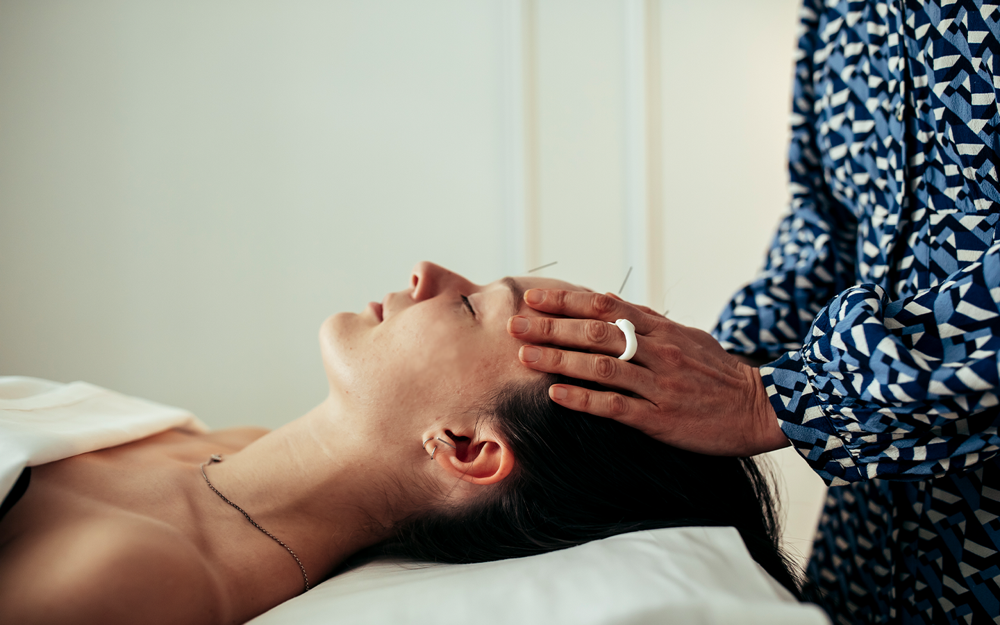 A practitioner pressing acupressure points on a woman's forehead during a facial treatment