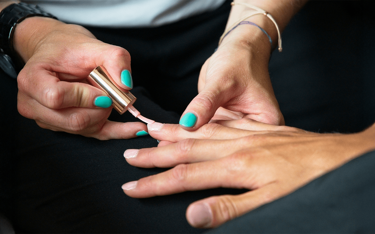 Manicurist applying light pink nail polish to a client's fingernails