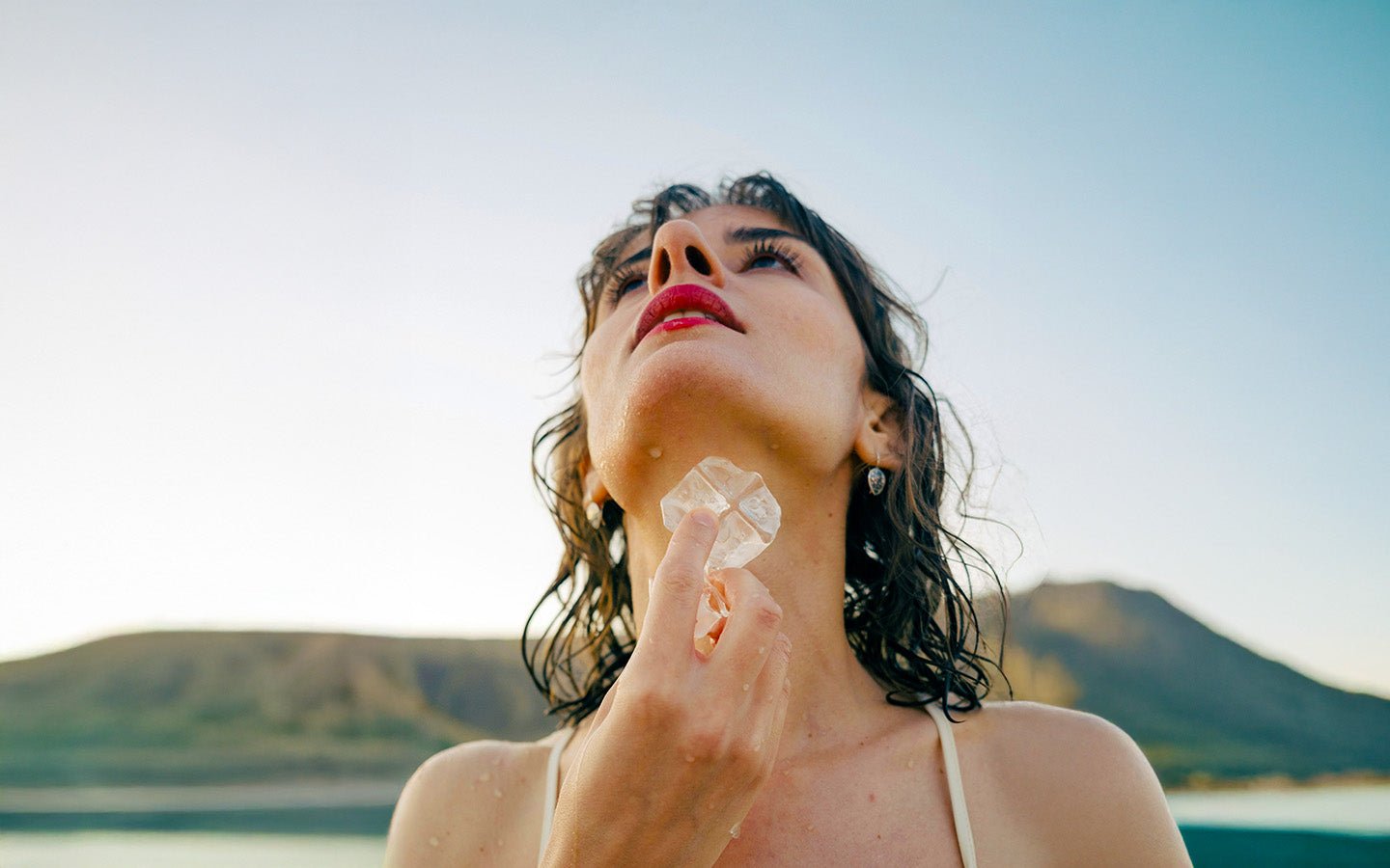 Woman with wet hair and red lipstick cooling her neck with ice outdoors