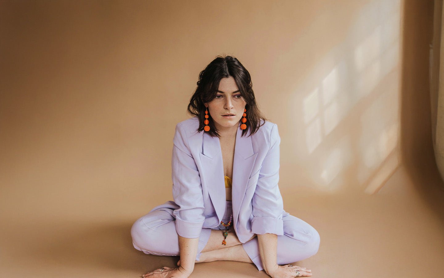 Woman in lavender suit and orange earrings sitting on a beige floor
