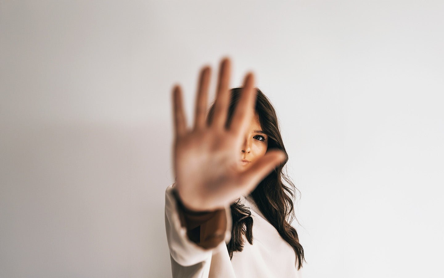 Woman with dark hair holds hand up to camera, light background