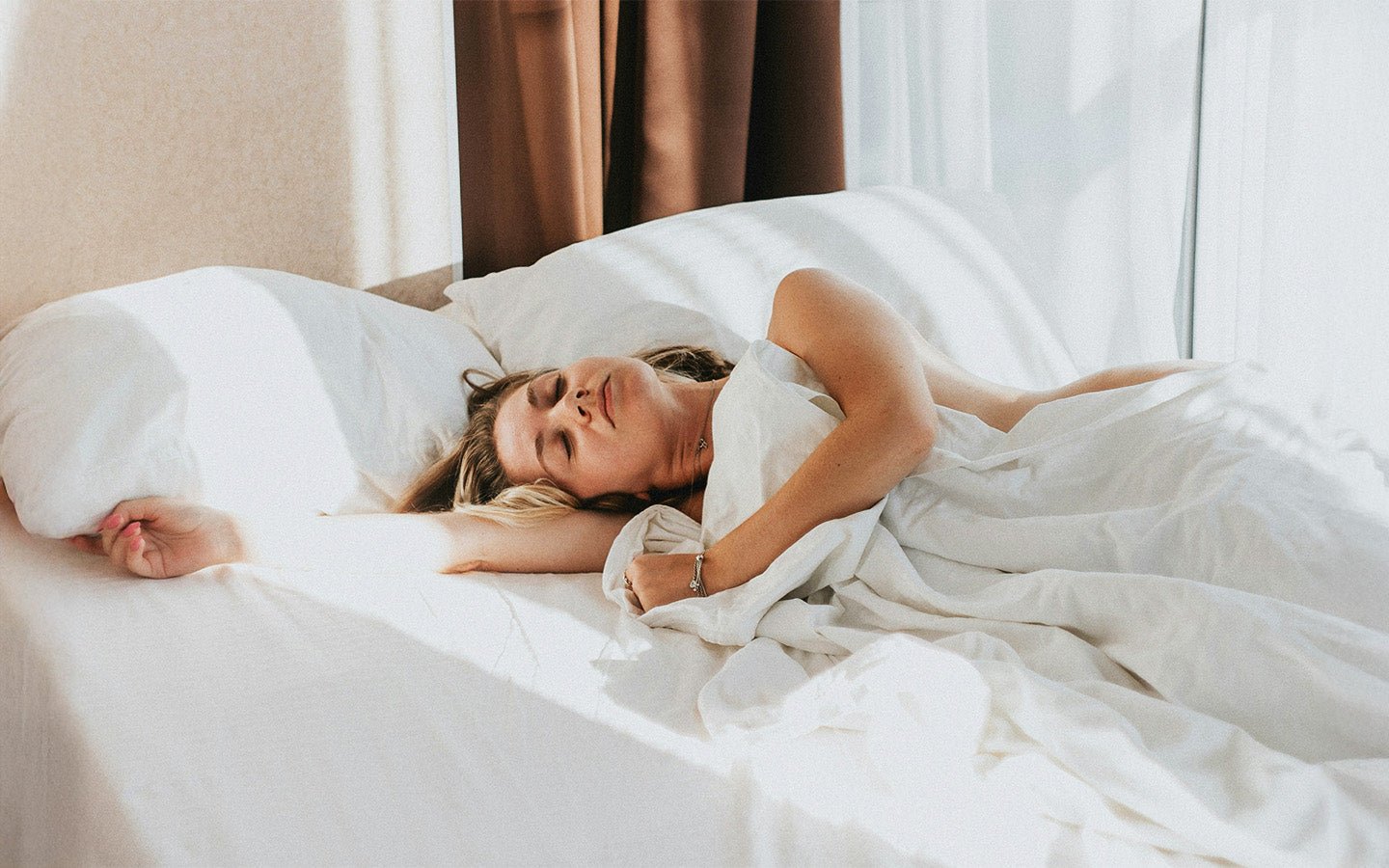 Woman sleeping peacefully in a white bed with sunlight streaming in