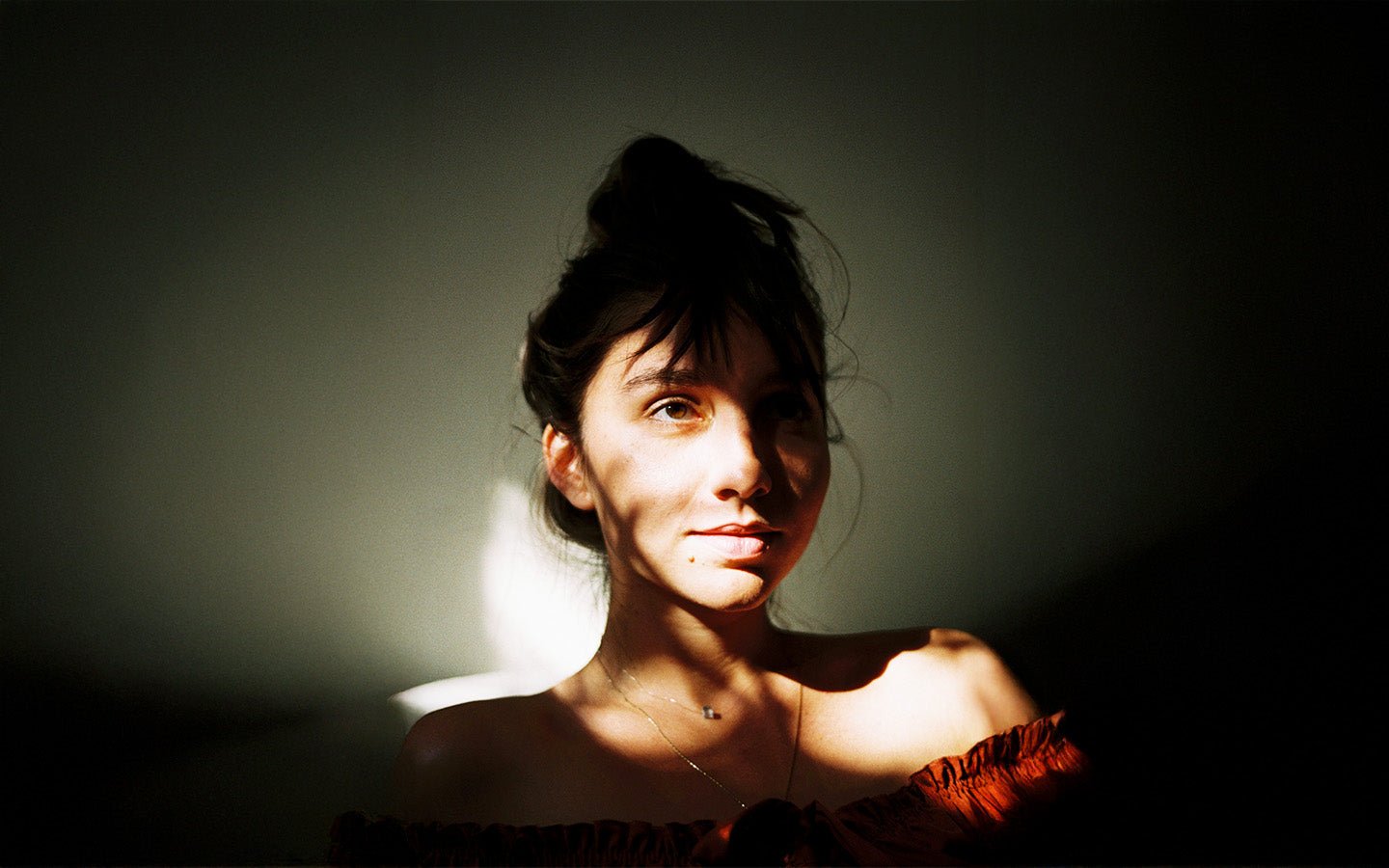 Woman with dark hair in a messy bun, lit by a diagonal beam of sunlight