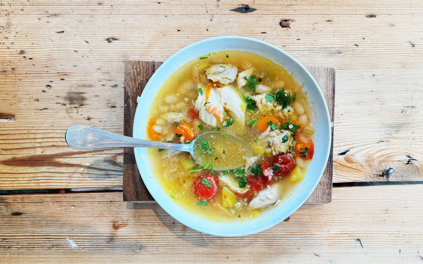 Bowl of chicken and vegetable soup with beans, carrots, and herbs, viewed from above