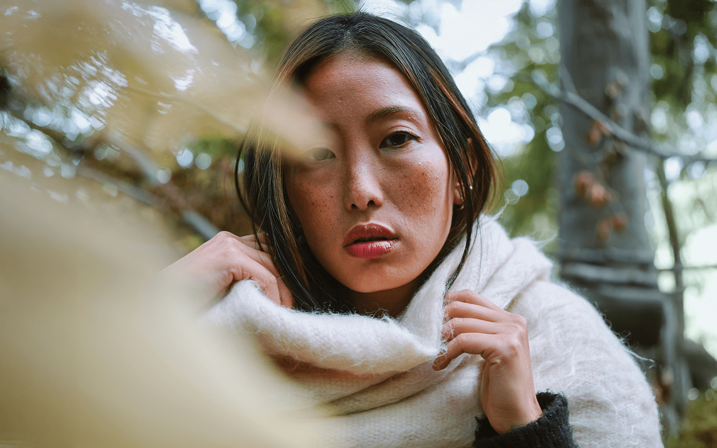 Woman with freckles in a white scarf, outdoors with blurred trees
