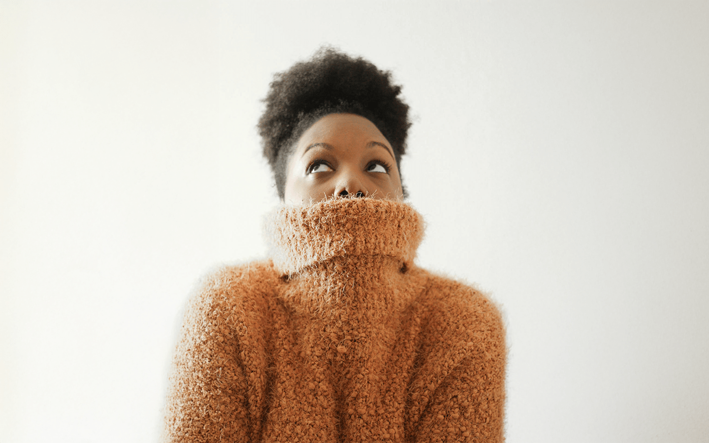 Woman in a fuzzy brown turtleneck looking up against a white background