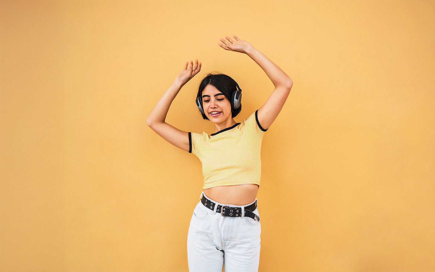 Young woman with headphones dancing against a yellow wall