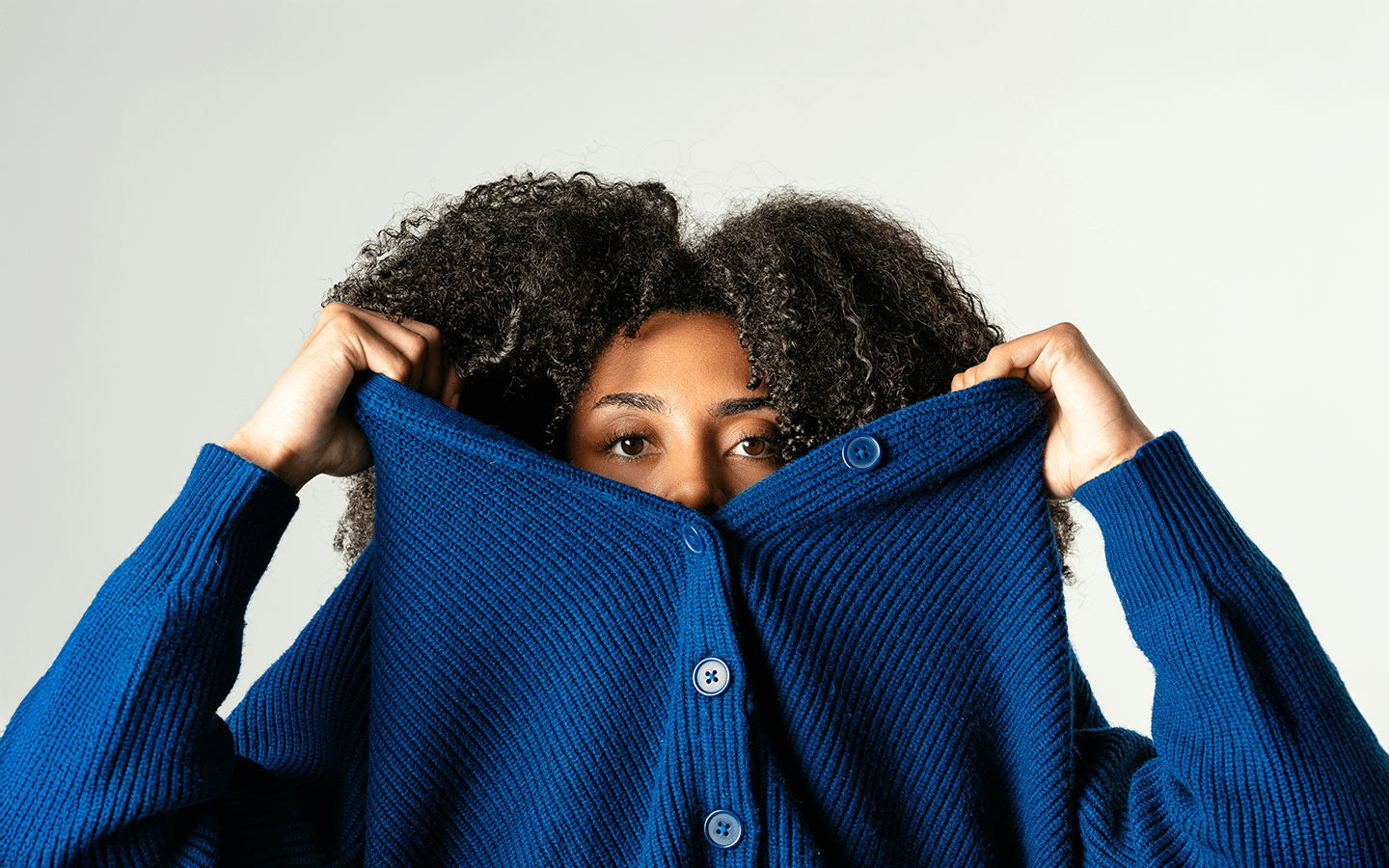 Woman with curly hair peeking over a blue cardigan