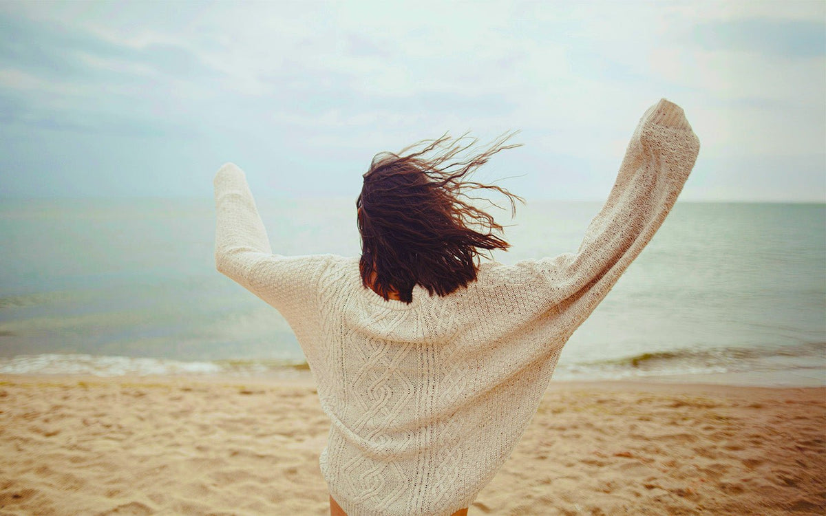 Woman in white sweater with arms raised on a sandy beach