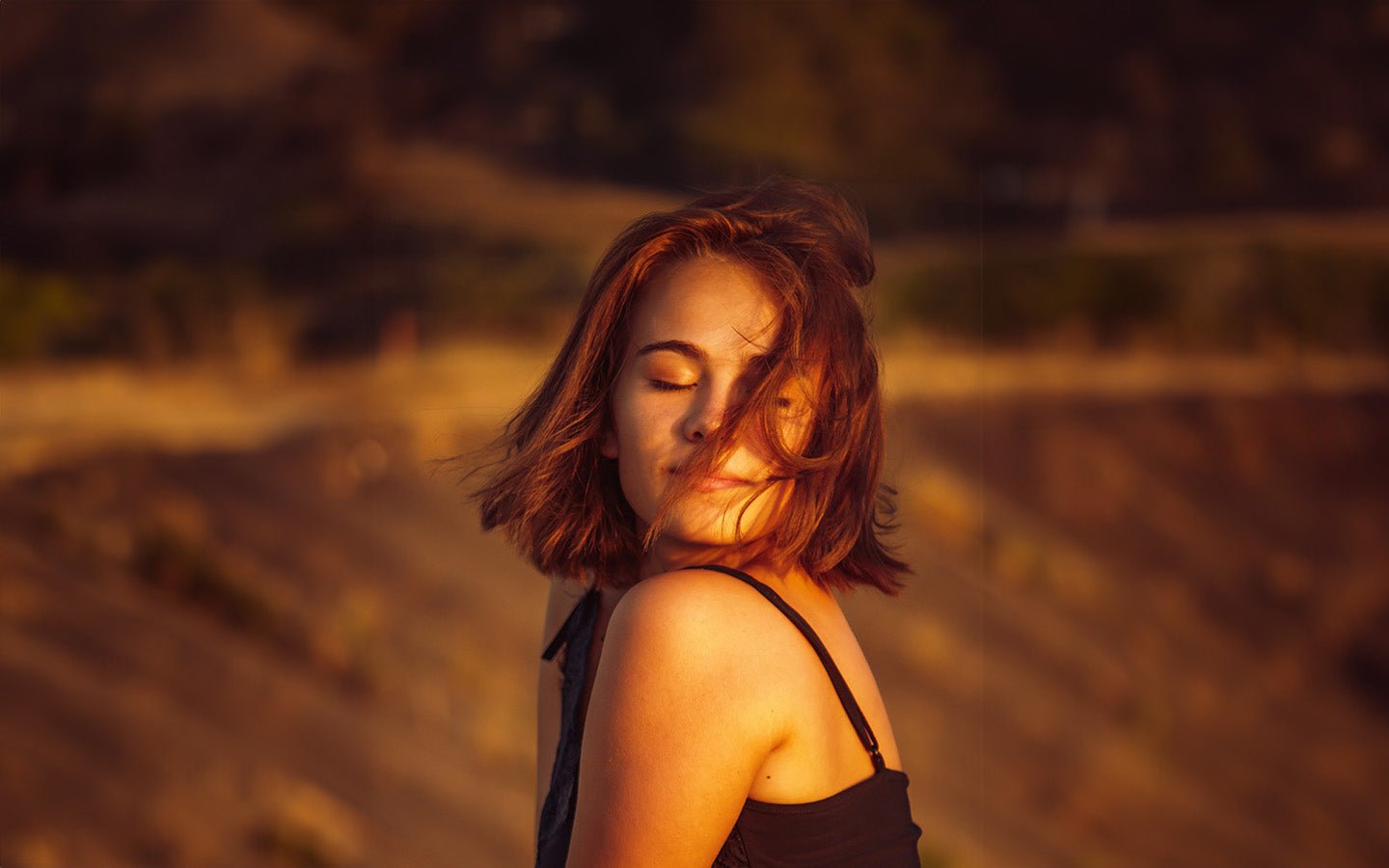 Woman with closed eyes, wind-swept hair, and sunlit skin in a natural setting
