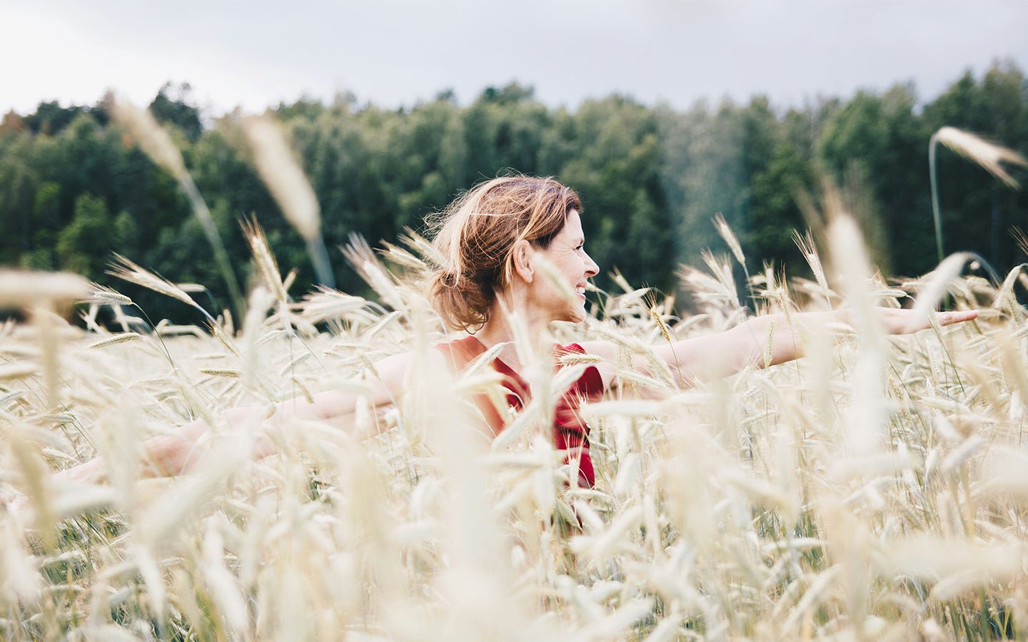 Woman in red shirt with arms outstretched in a field of tall, light-colored grass