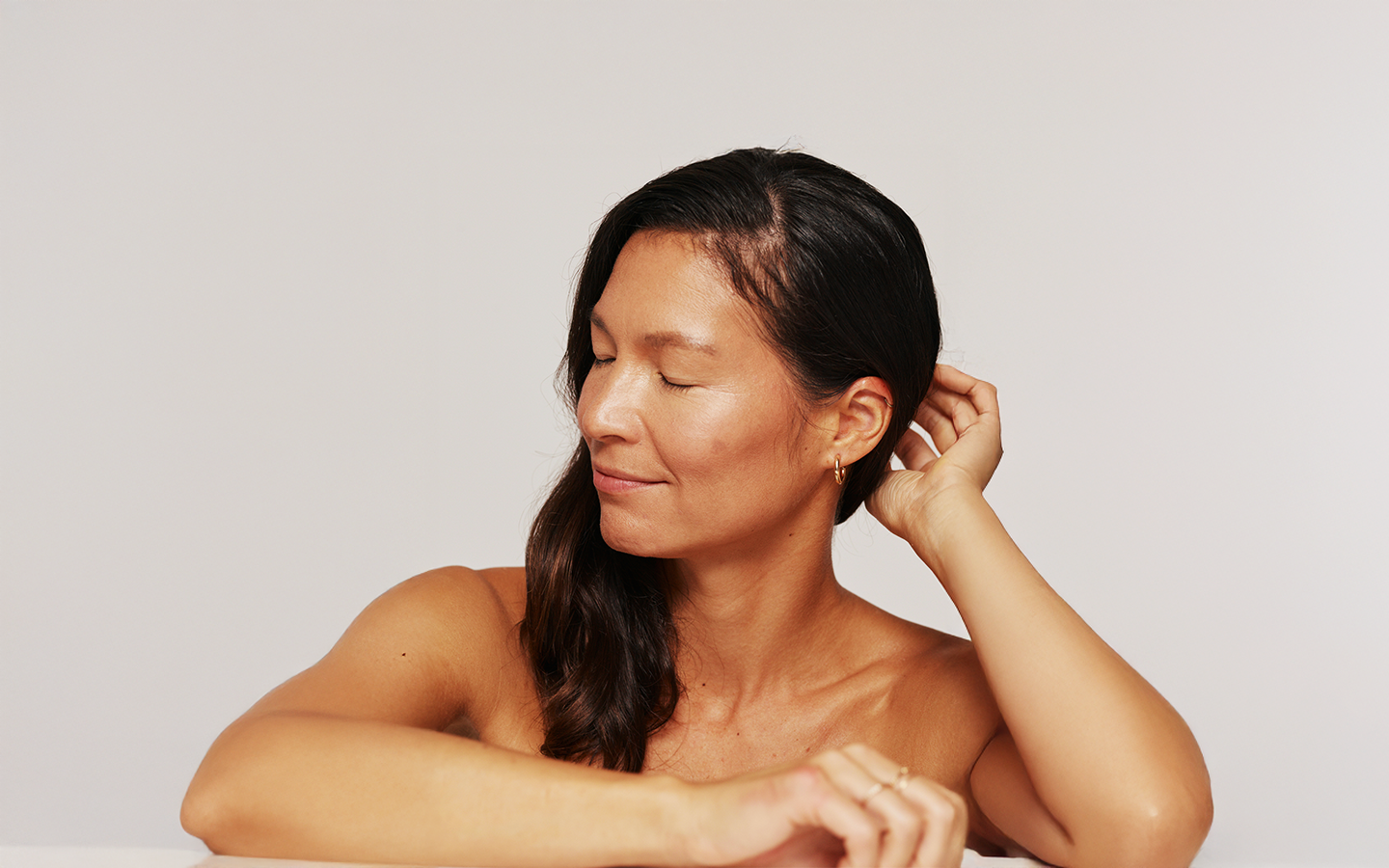 Woman with eyes closed in warm natural light, touching her hair, listening to her body