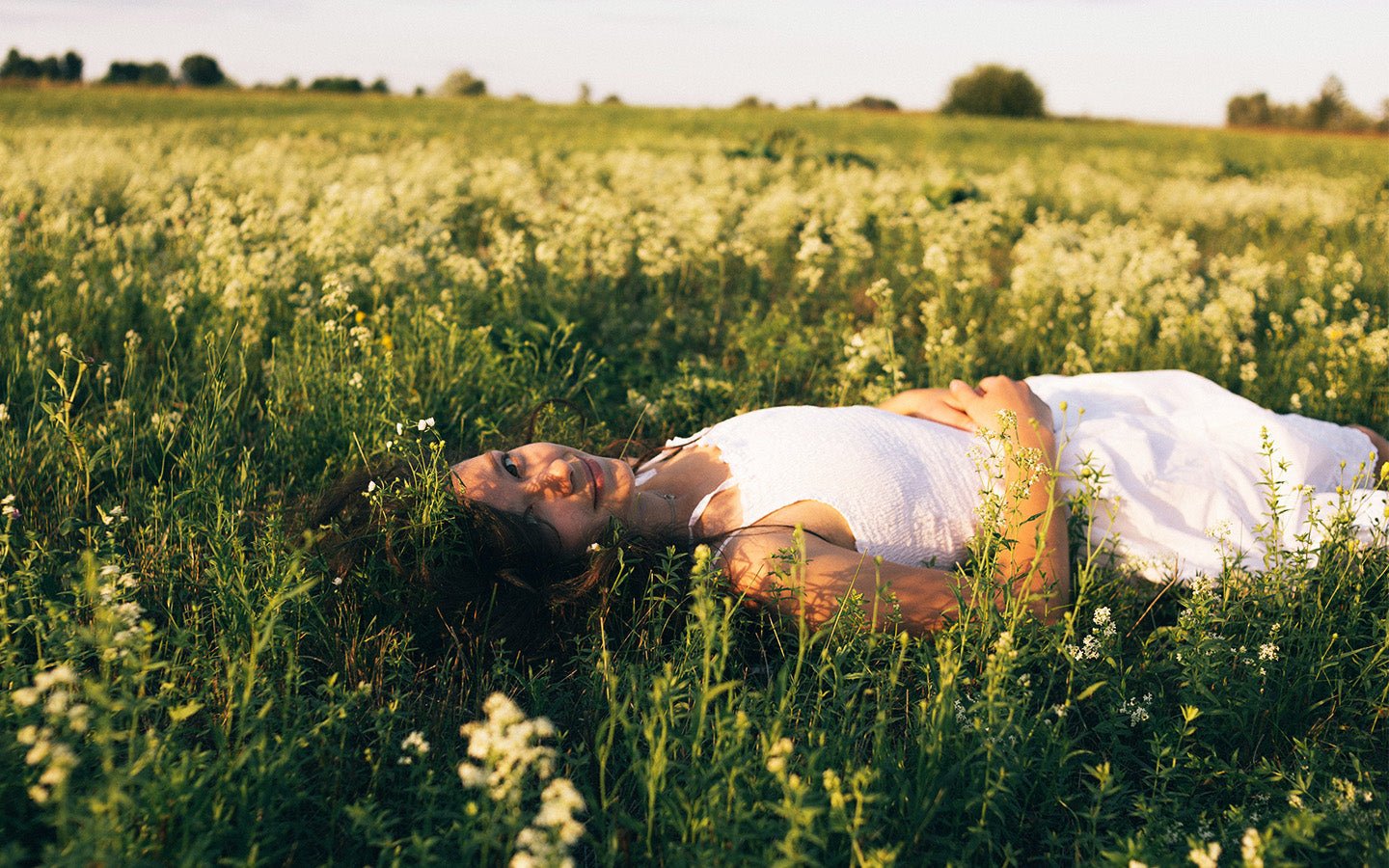 Woman in white dress lying in a field of green grass and white flowers